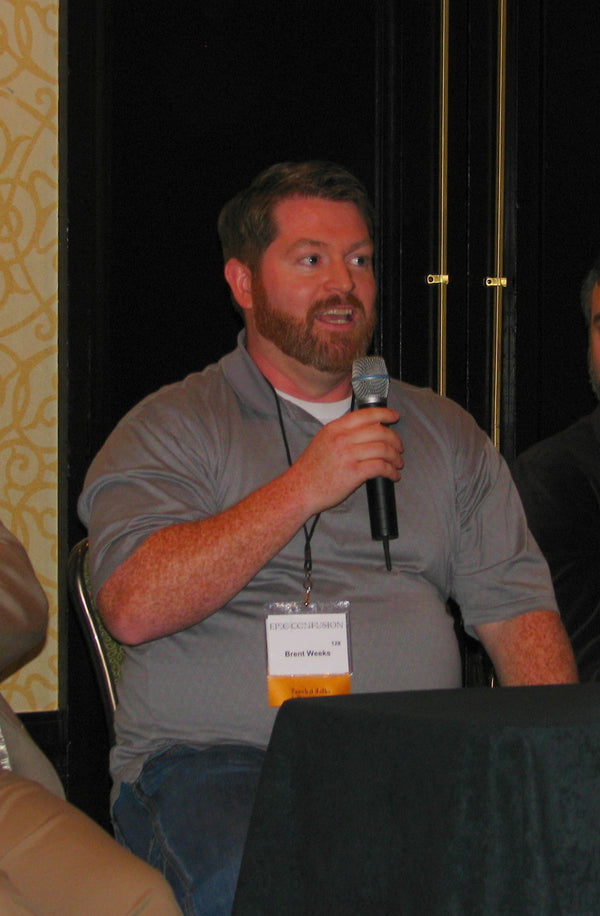 Man speaking into a microphone at an event with a name tag