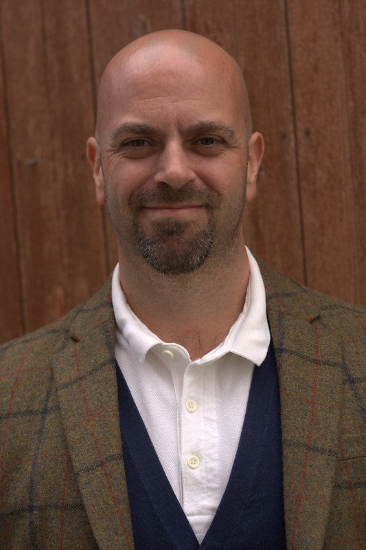 Man wearing a tweed jacket over a white shirt with a wooden background