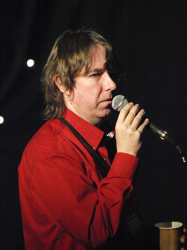 Man in a red shirt holding a microphone against a dark background