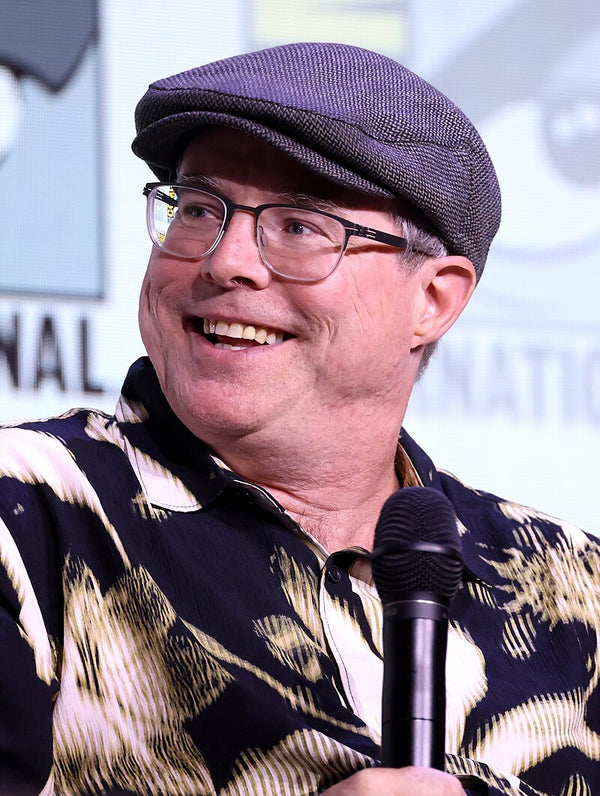 Man with glasses and a cap speaking into a microphone at an event.