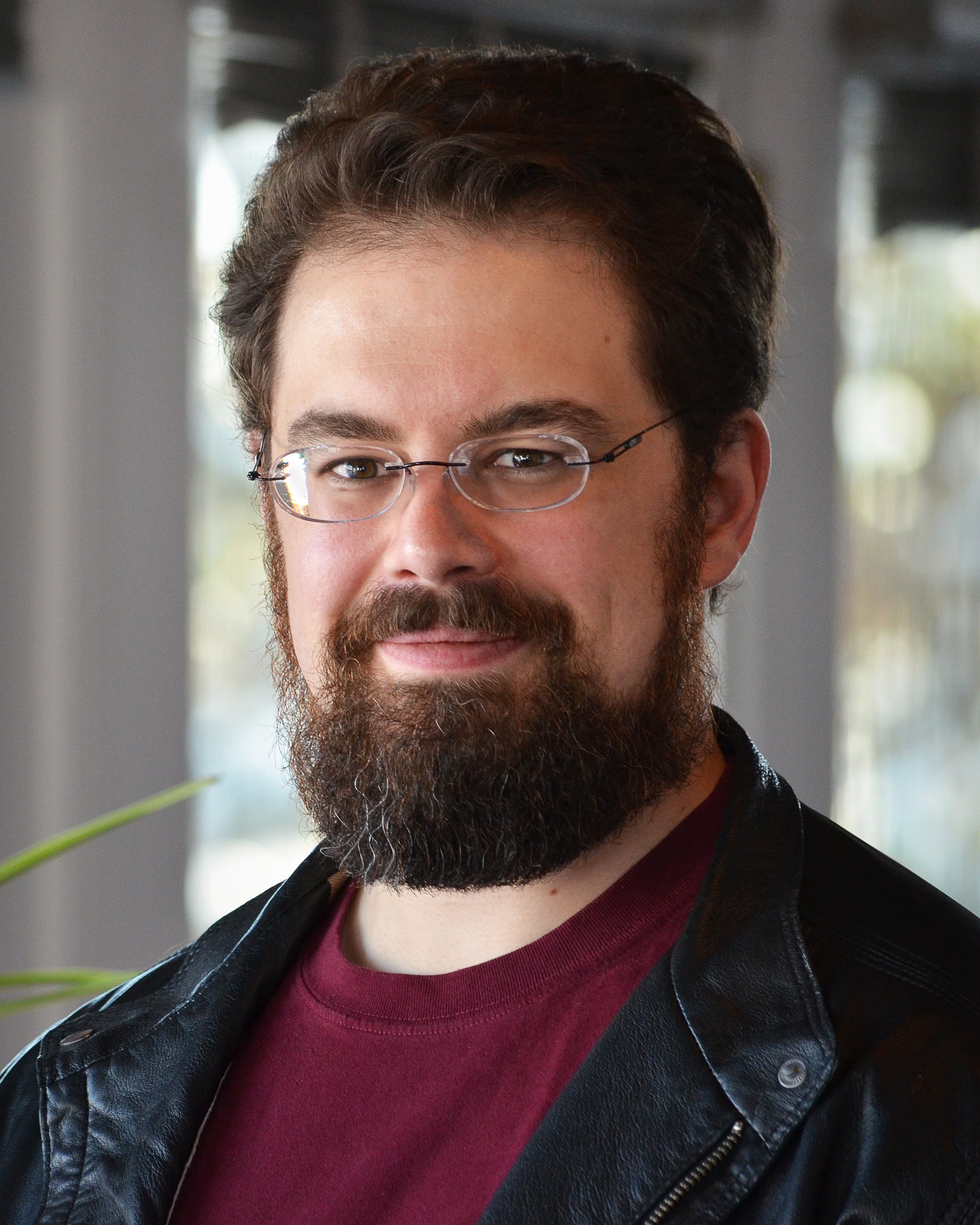 Man with glasses and a beard wearing a black jacket over a red shirt.
