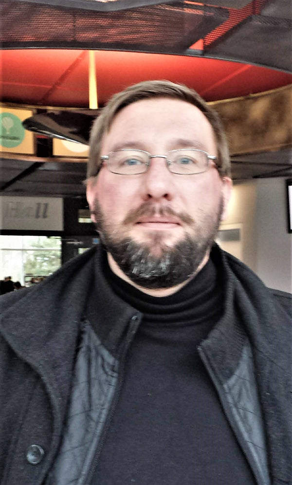 Man wearing glasses and a dark coat in an indoor setting