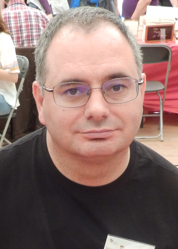 Man wearing glasses and a black shirt in an indoor setting with people and chairs in the background