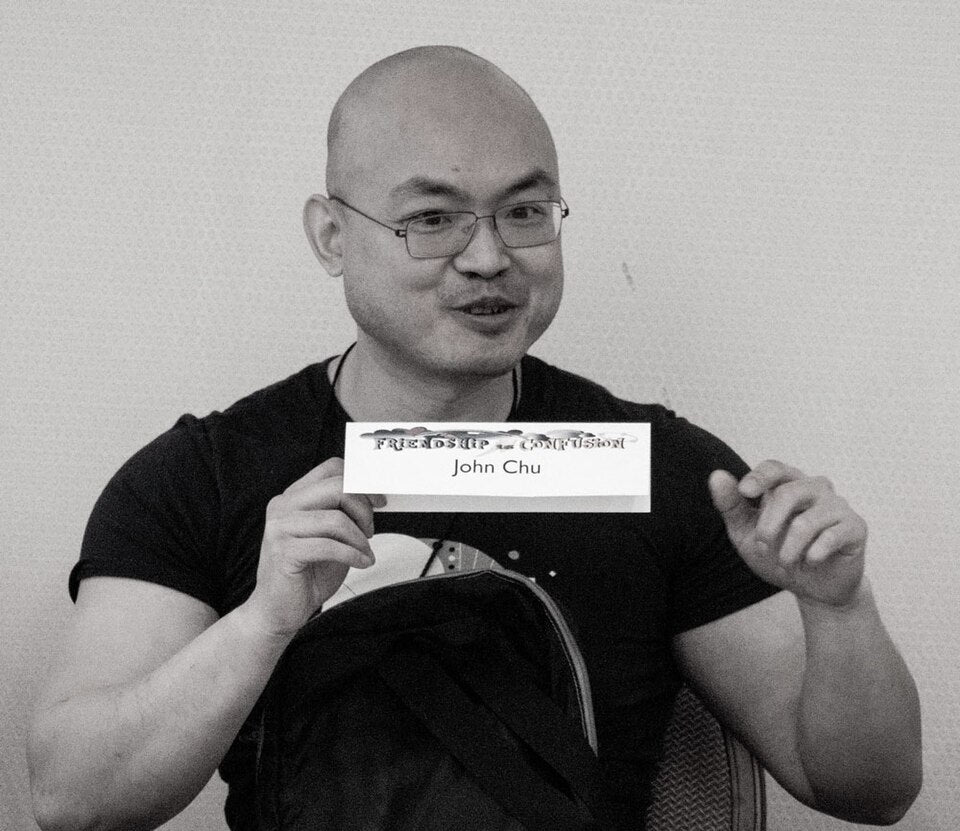 Person holding a card with 'John Chu' on it against a plain background