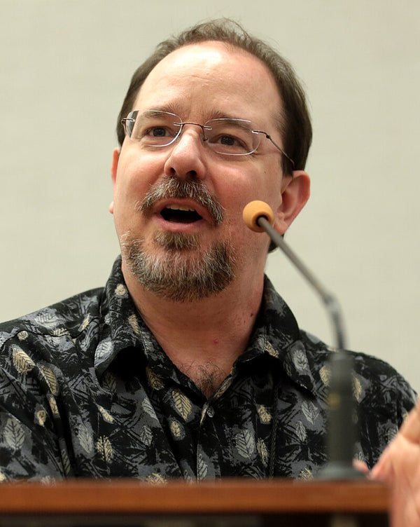 Man with glasses and a microphone speaking at a podium