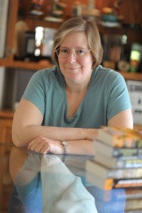 Woman with glasses sitting at a table with books, smiling.