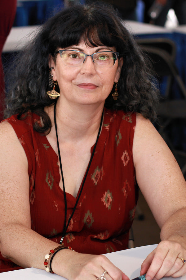 Woman wearing glasses and a red patterned top sitting at a table.