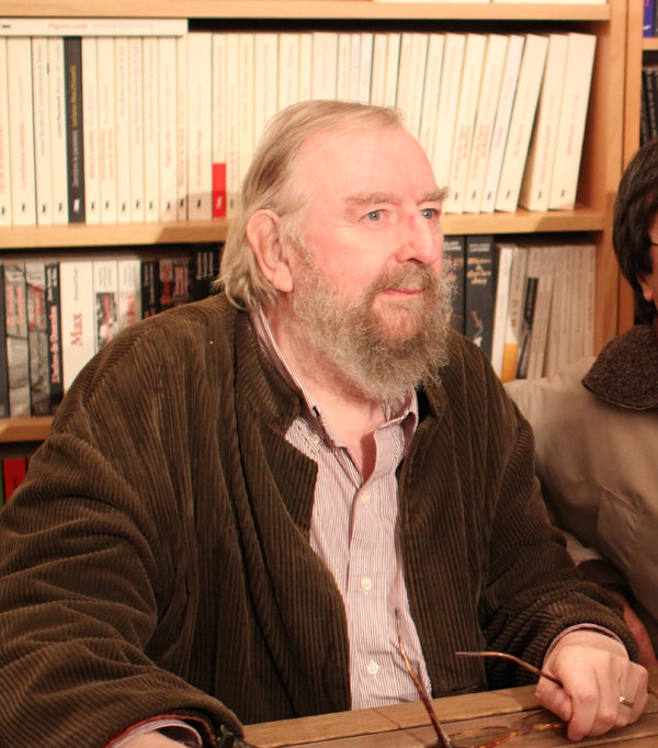 Man with a beard sitting at a table in front of a bookshelf