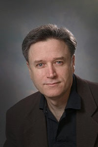 Man wearing a brown jacket over a black shirt against a gray background