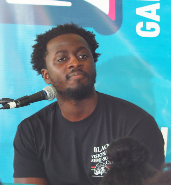 Man speaking into a microphone with a blue background and 'GQ' logo.