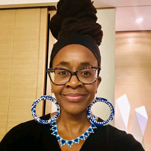Woman wearing glasses and large hoop earrings with a blue and white pattern, indoors.