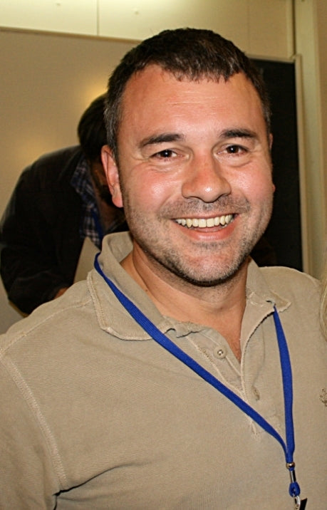 Man wearing a beige shirt with a blue lanyard around his neck, smiling.