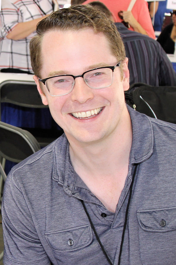 Man wearing glasses and a gray shirt in an indoor setting with blurred background