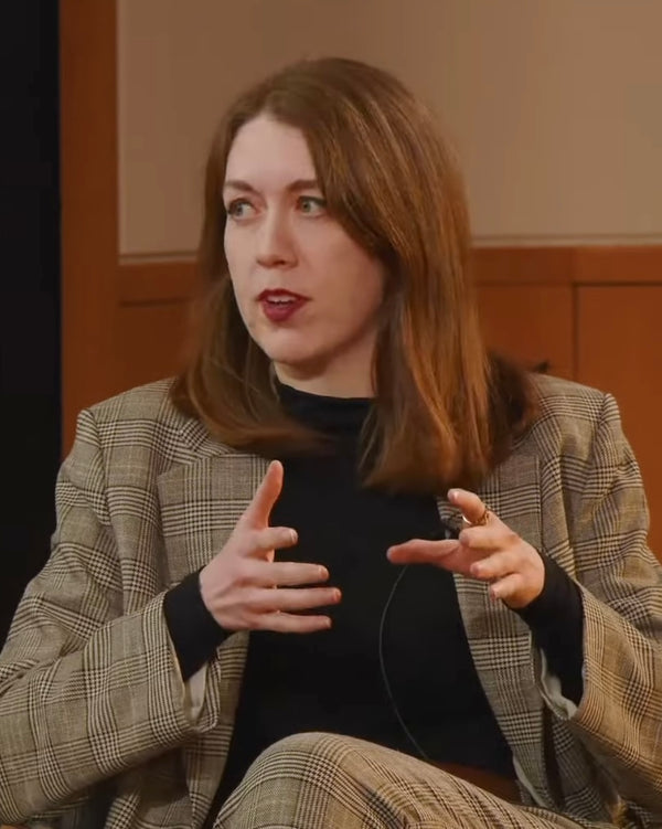 Woman in a plaid jacket speaking with expressive hand gestures.