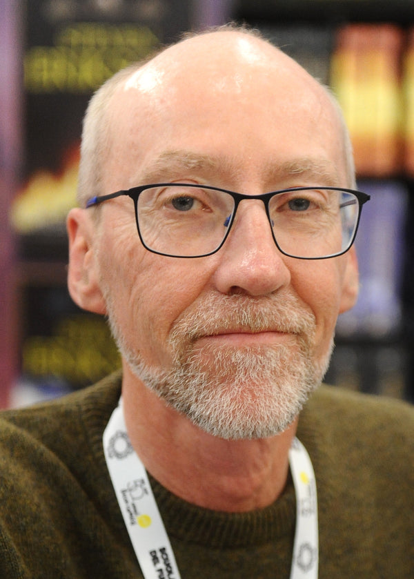 Man with glasses and a beard wearing a brown sweater with a blurred background
