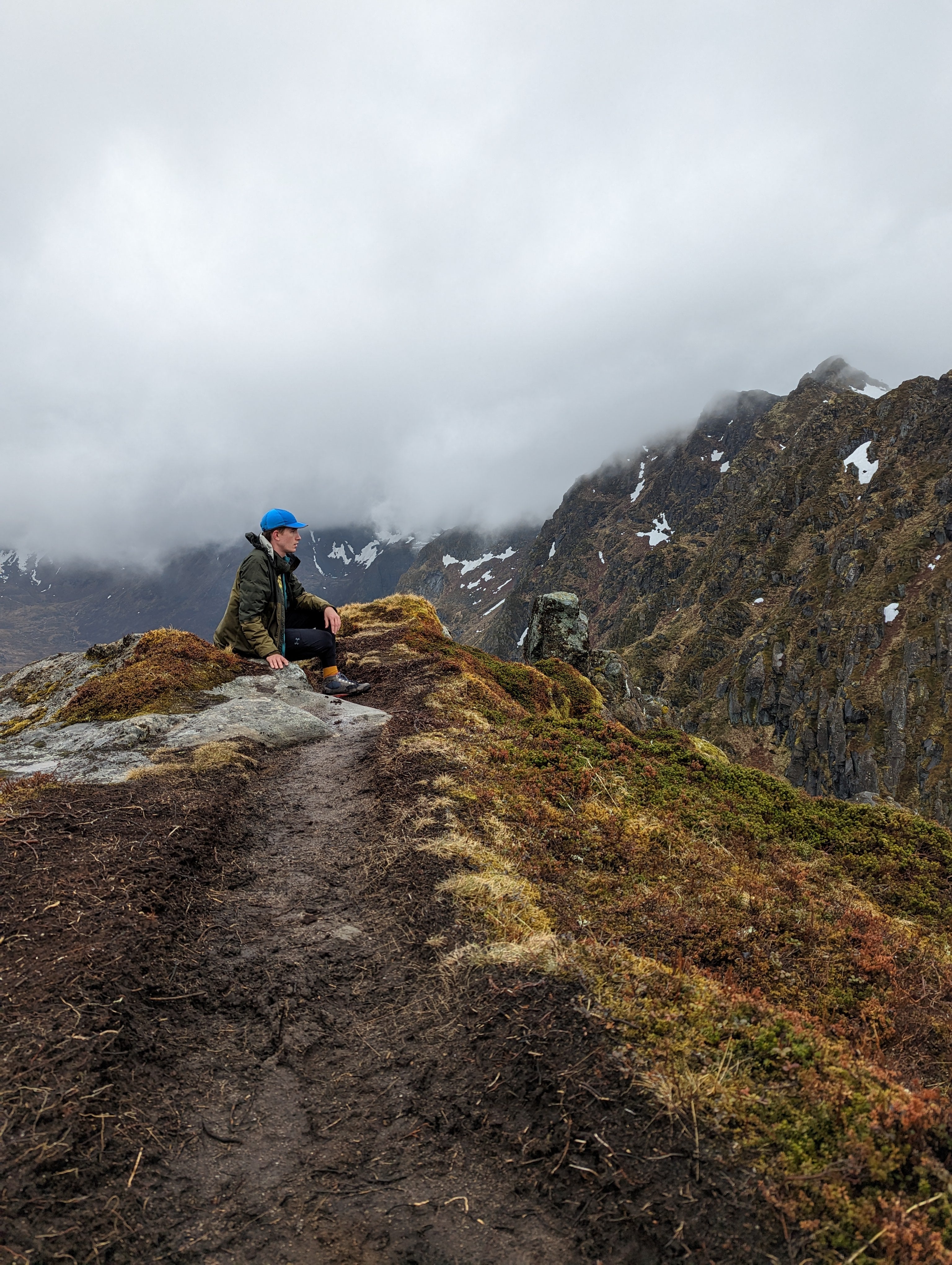 Person sitting on a mountain trail with foggy mountains in the background