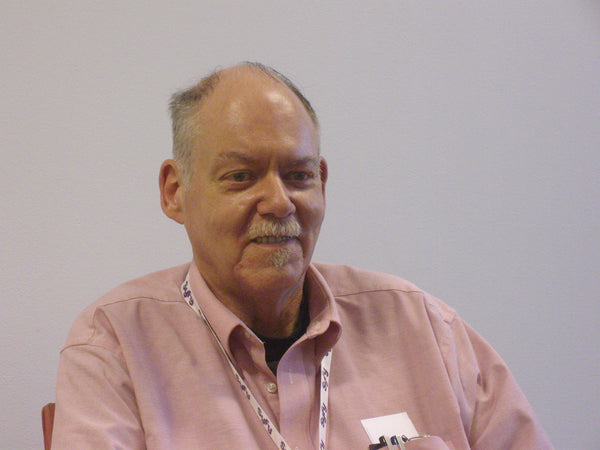 Man wearing a pink shirt with a lanyard against a plain background